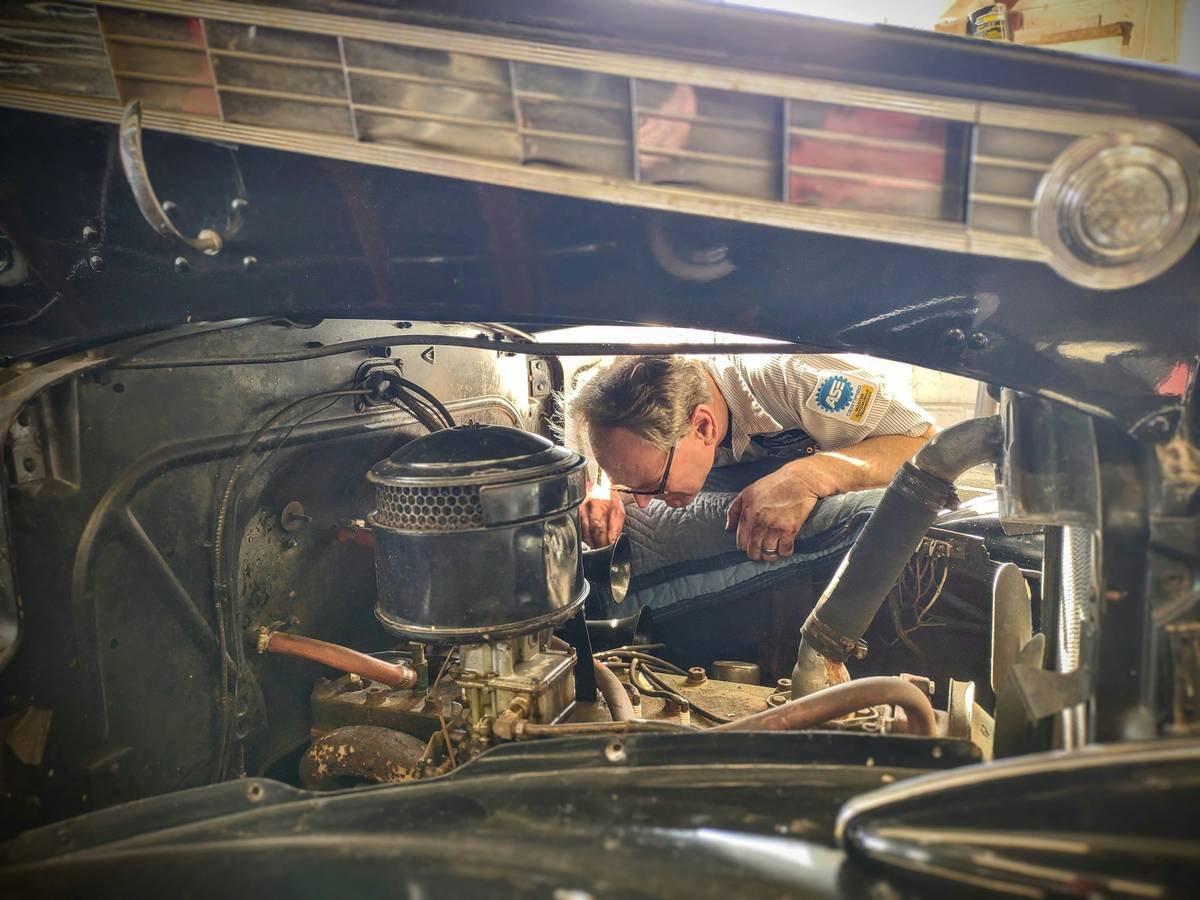 Mechanic inspecting a car's exhaust system under a lift at an auto shop.